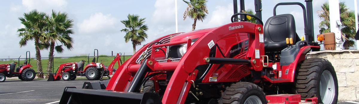 Mahindra® tractor parked outside in a lot with other tractors and palm trees in the background